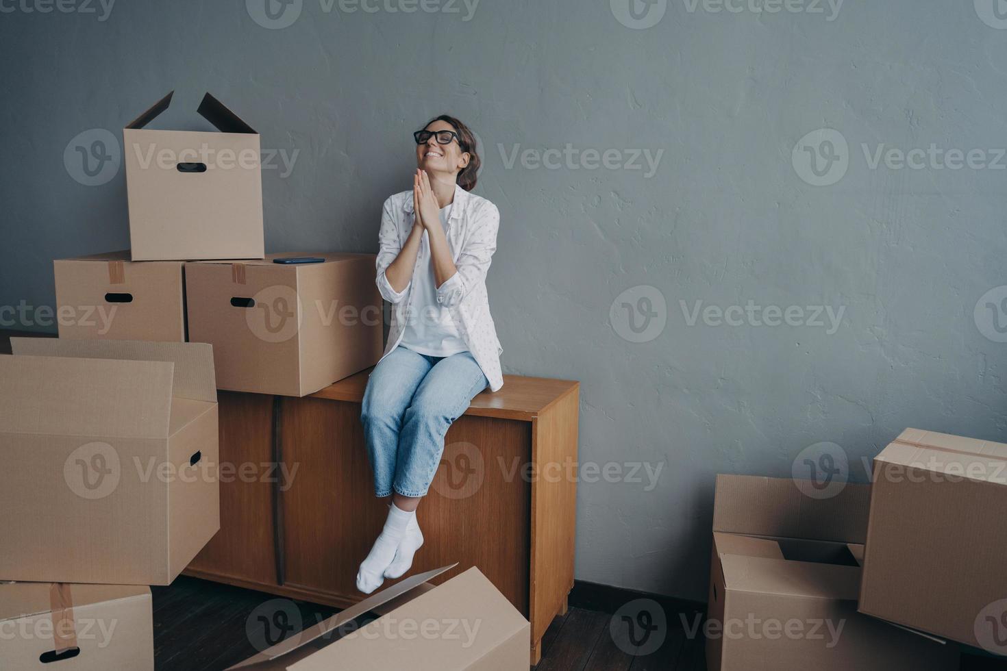 Happy young european woman purchases real estate. Thanks god. Girl is sitting on boxes and dreaming. photo