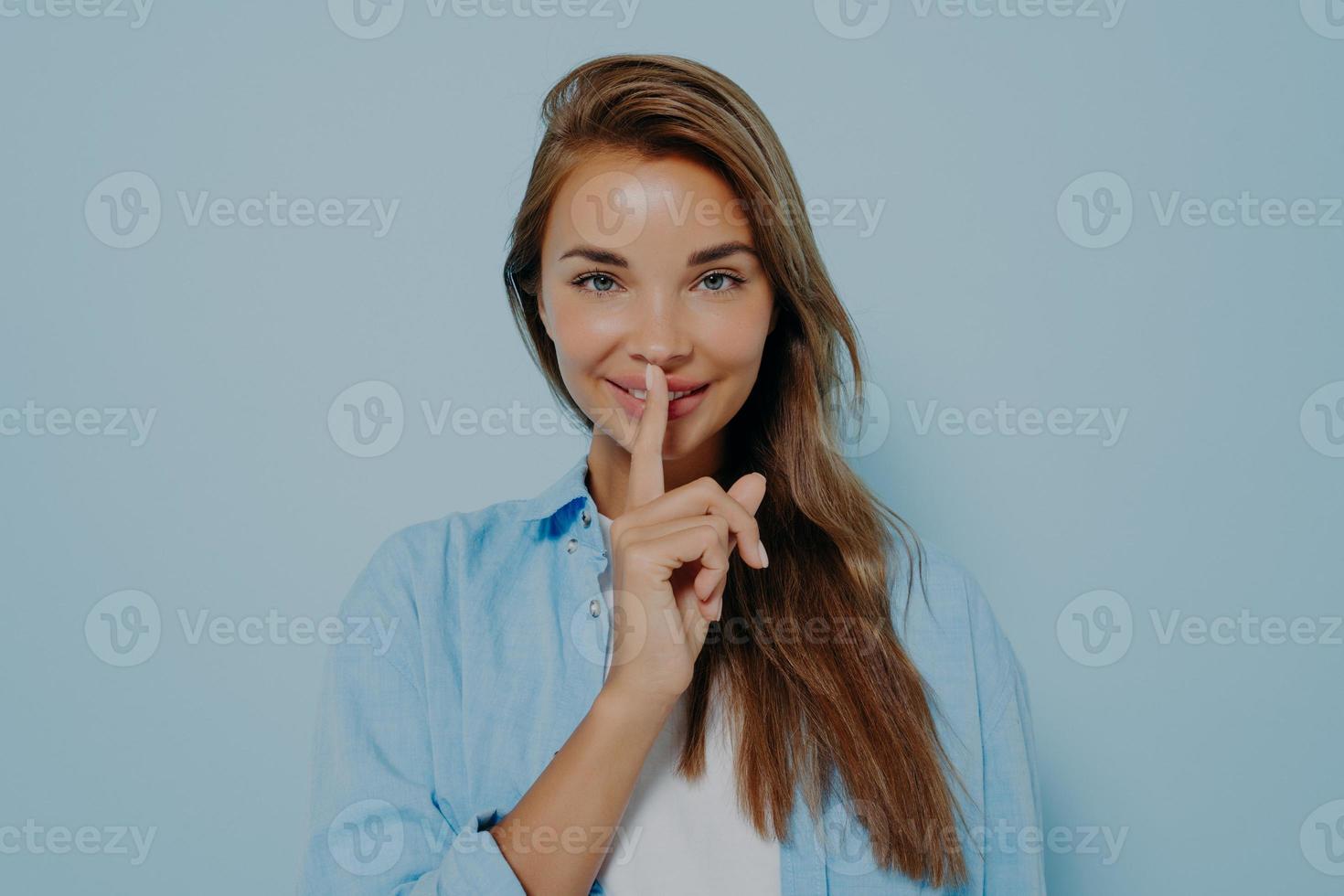 Beautiful woman showing shush gesture on light blue background photo