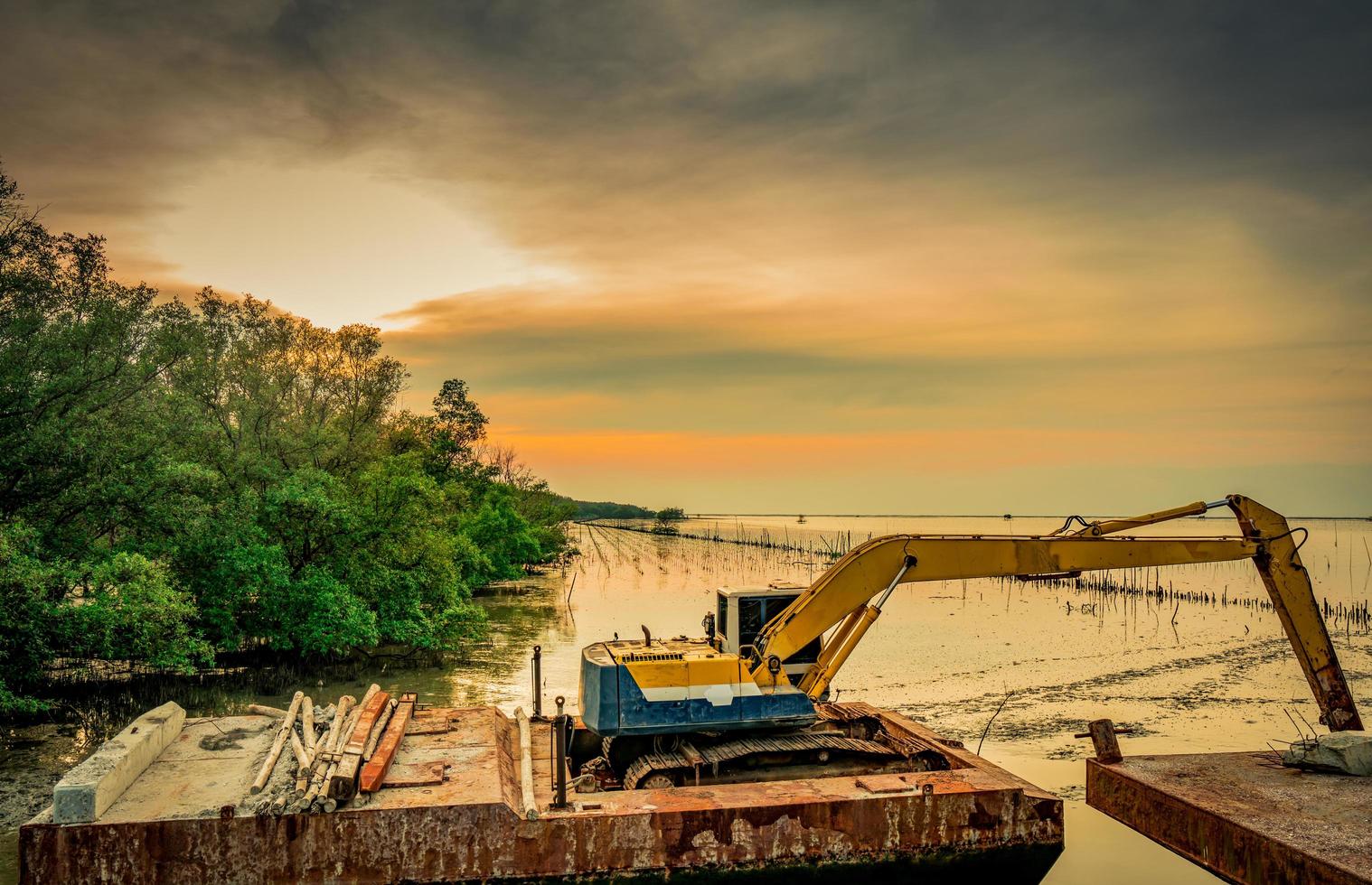 The backhoe is digging along the sea shore near the mangrove forest to place the pipe. Beautiful clouds and sky at construction site photo
