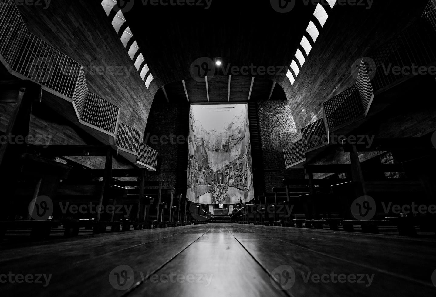 Perspective view in church. A few people sit on wooden bench with many of empty bench in church on Sunday. Black and white scene of wooden building interior with ceiling lamp. Europe architecture. photo