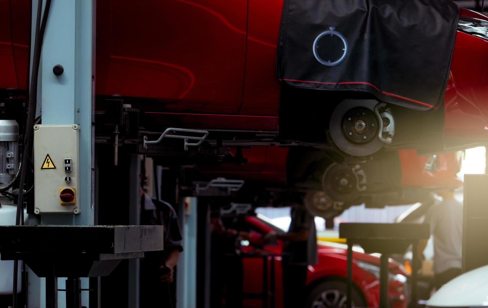 Selective focus on lift in auto repair shop. Red SUV car lifted in the garage for repair and maintenance service. Car check-up at service station by mechanic technician. Car body lifted in workshop. photo