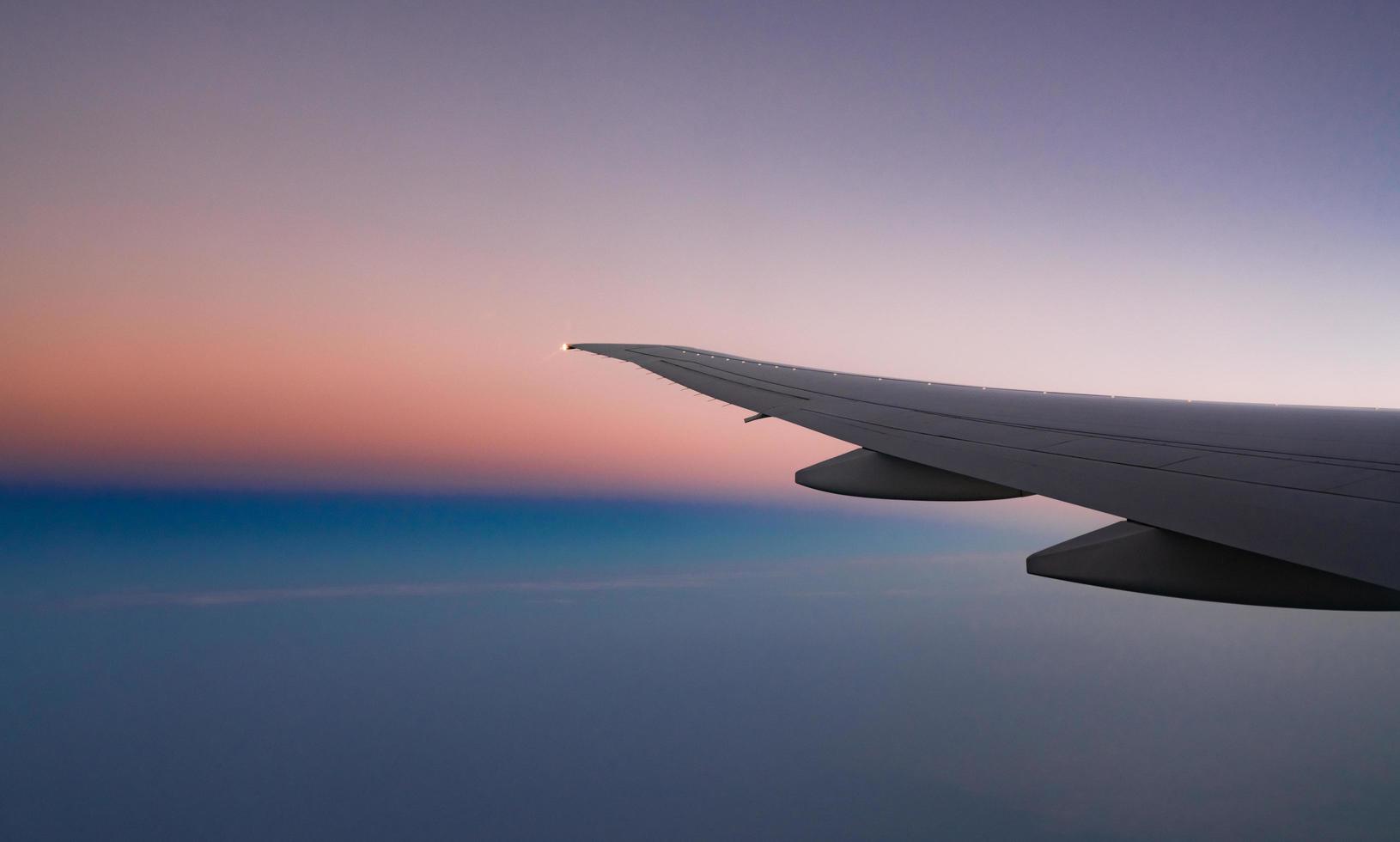 Wing of plane with beautiful sunrise skyline. Airplane flying on blue, purple, orange sky. View from airplane window. Commercial airline flight in the morning with sunlight. Plane wing above clouds. photo