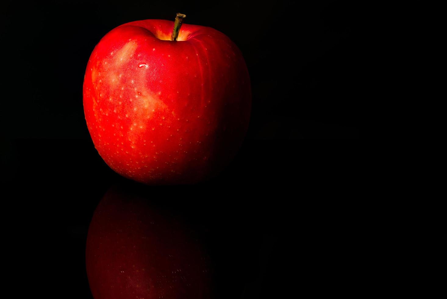 A red apple with water drops on skin isolated on black background with copy space. Healthy fruit and healthy food concept. Vegan food. photo