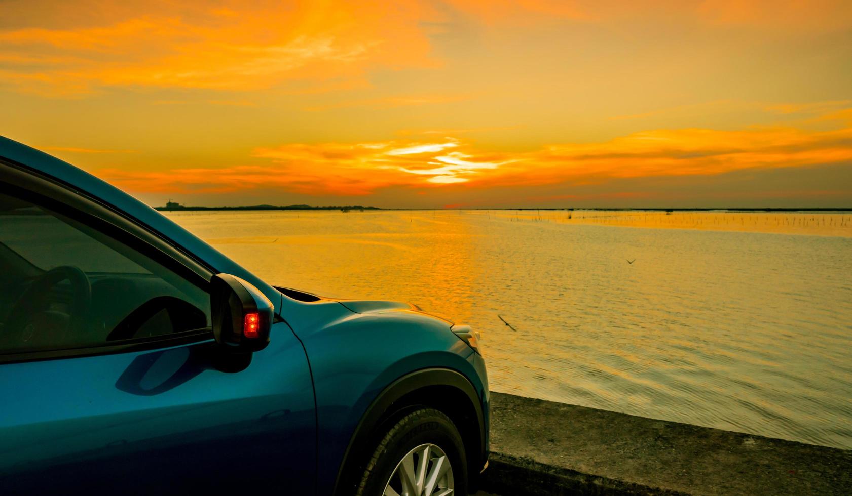 camión suv compacto azul con diseño deportivo y moderno estacionado en una carretera de hormigón junto al mar al atardecer. tecnología respetuosa con el medio ambiente. concepto de éxito empresarial. foto