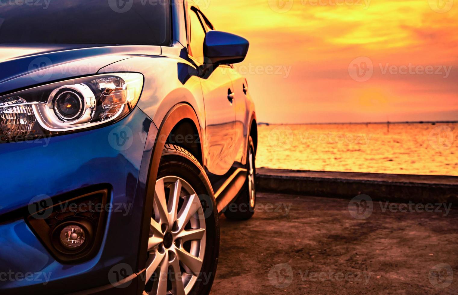 coche todoterreno de lujo aparcado en el aparcamiento junto a la playa al atardecer. vista frontal del nuevo camión suv con diseño deportivo y moderno y hermoso cielo dorado de puesta de sol. viaje por carretera en vacaciones de verano. vehículo eléctrico. foto