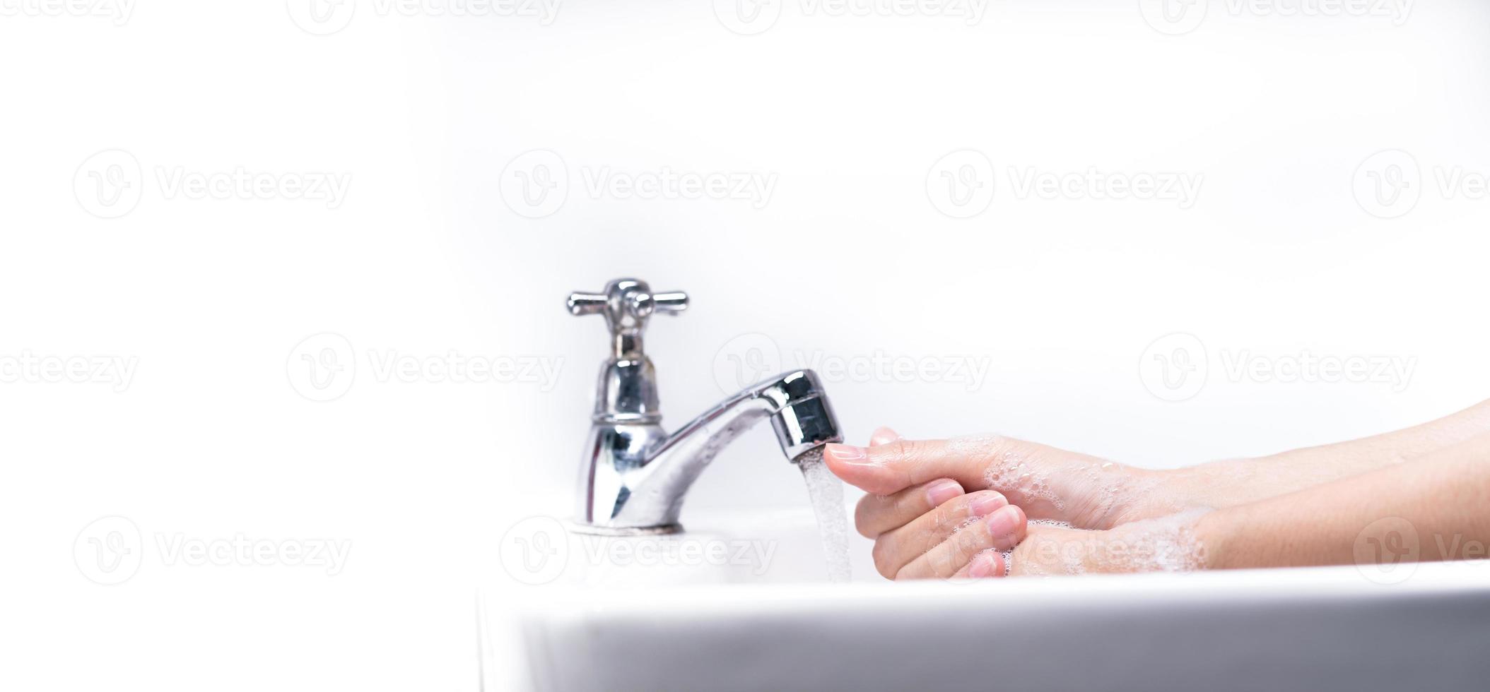 Woman washing hand with soap foam and tap water in bathroom. Hand clean under faucet on sink for personal hygiene to prevent flu and coronavirus. Good procedure of hand wash to kill bacteria, virus. photo