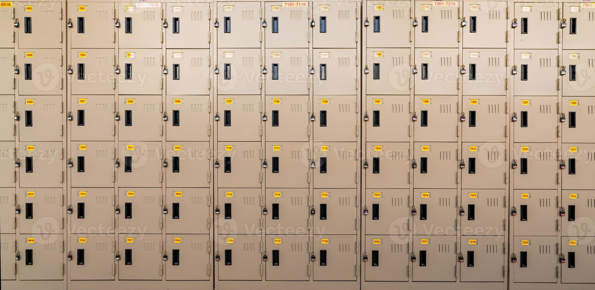 Closeup beige locker with lock and numbered yellow tags at locker room. Locker for safety and security storage. Row of locker with locked door background. photo