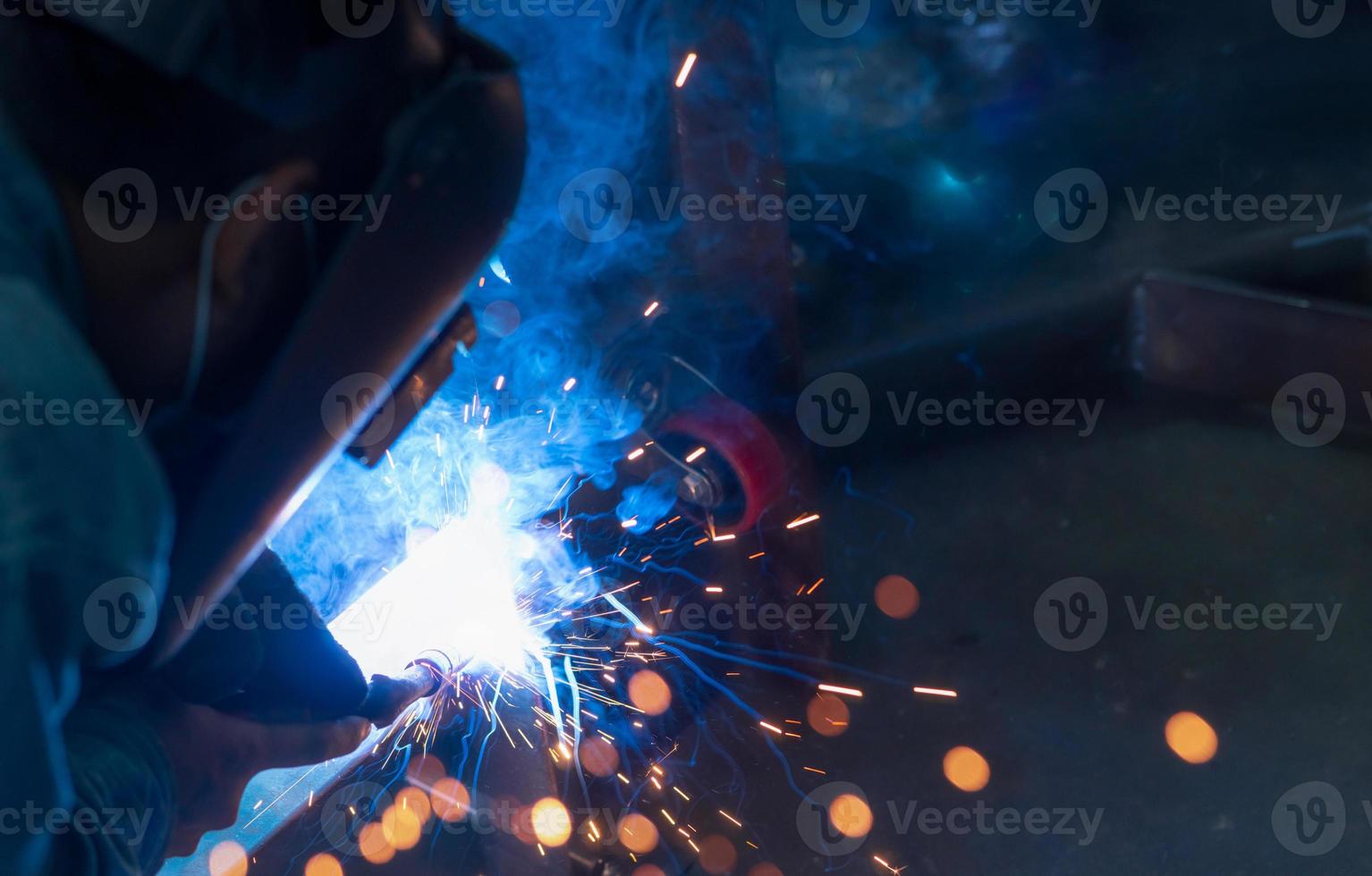 Welder welding metal with argon arc welding machine and has welding sparks. A man wears a welding mask. Safety in industrial workplace. Welder working with safety. Steel industry technology. photo