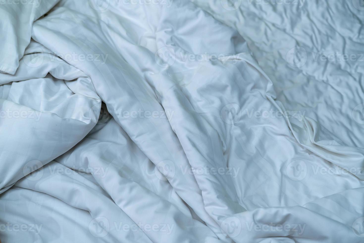 White linen blanket in hotel bedroom. Close up detail of messy white blanket after waking up in morning. Comfortable bed with soft white duvet. Sleep tight with good quality bedding household concept. photo