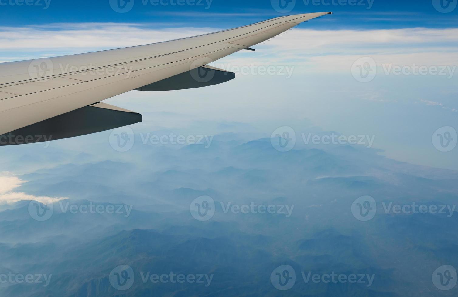 Wing of plane over mountain. Airplane flying on blue sky and white clouds. Scenic view from airplane window. Commercial airline flight. Plane wing. Flight mechanics concept. International flight. photo