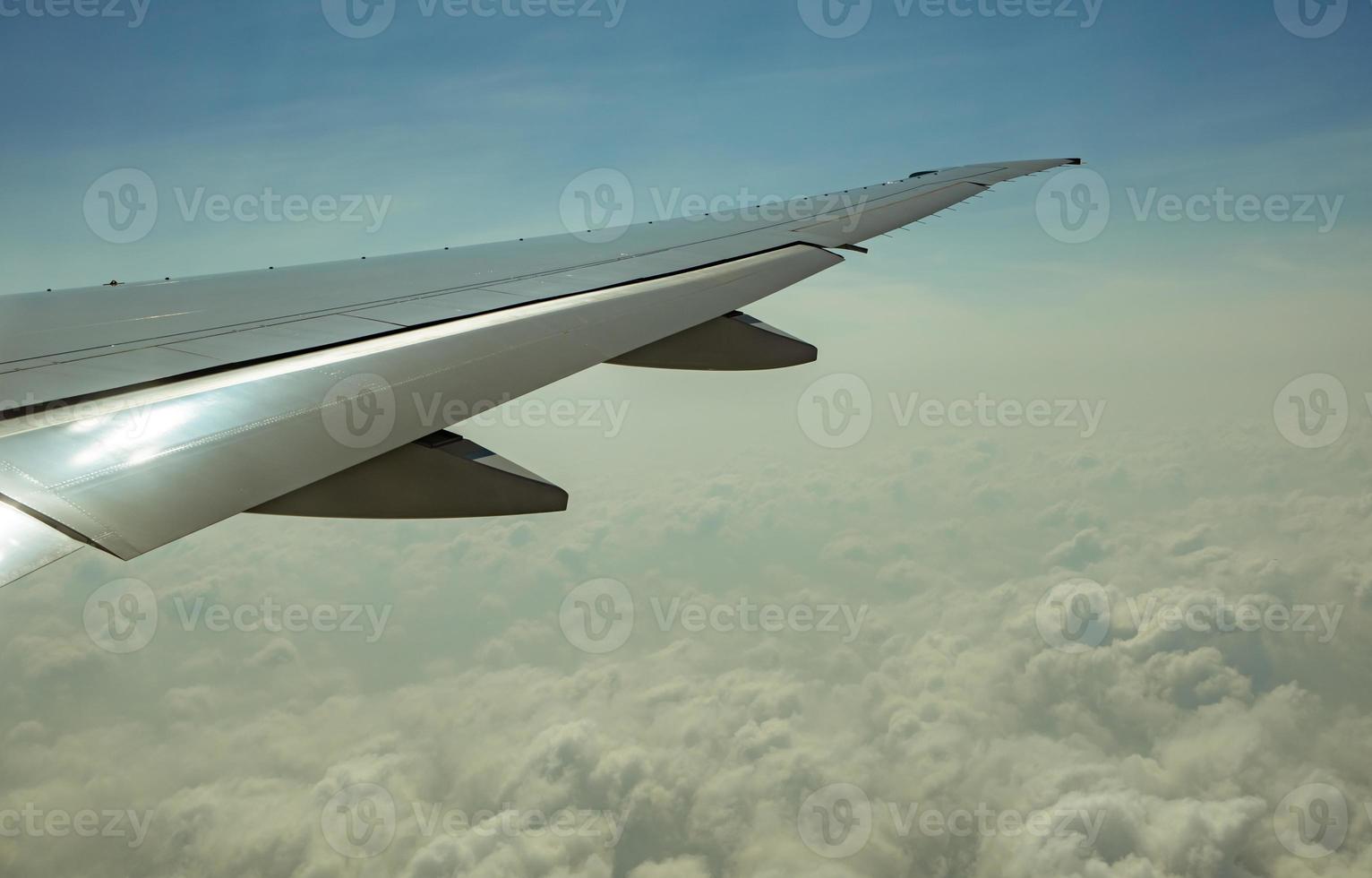 Wing of plane over white clouds. Airplane flying on blue sky. Scenic view from airplane window. Commercial airline flight. Plane wing above clouds. Flight mechanics concept. International flight. photo