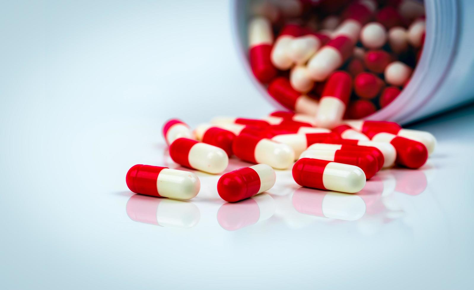Red-white capsule pills on white table on blurred background of drug bottle. Antibiotics drug resistance. Antimicrobial capsule pills. Pharmaceutical industry. Pharmacy. Global healthcare concept. photo
