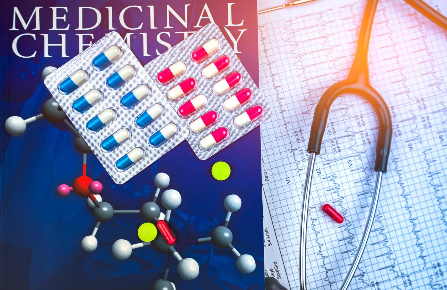 píldoras en el libro de texto de química médica y estetoscopio puesto en papel de informe gráfico de electrocardiograma ekg o ecg. concepto de investigación de la estructura del fármaco. concepto de cardiología y resistencia a los antibióticos. foto