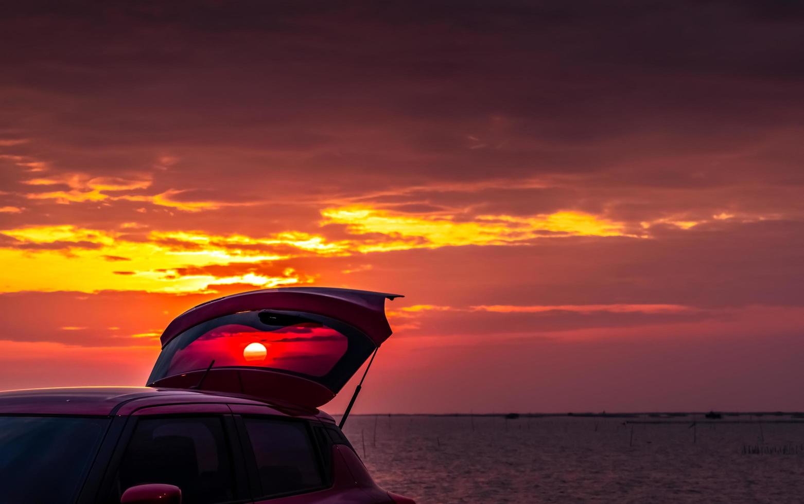 coche todoterreno rojo con diseño deportivo con camión abierto estacionado en una carretera de hormigón junto al mar en el cielo del atardecer. tecnología y negocios de automóviles eléctricos. automóvil híbrido y automotriz. viaje tropical por carretera. foto