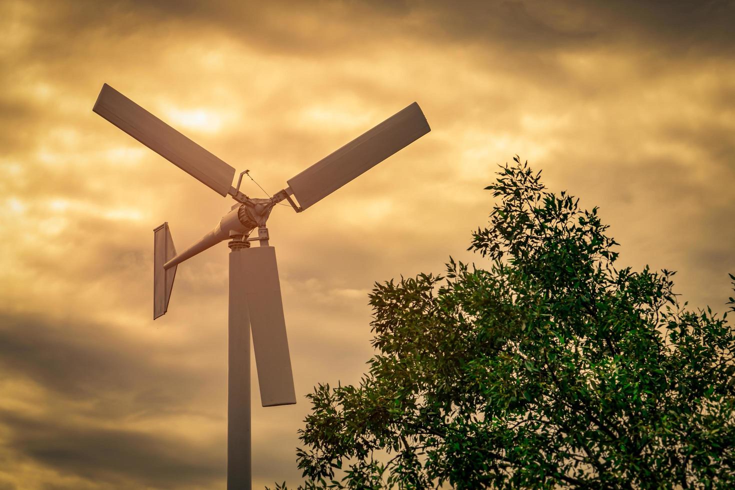 Horizontal axis wind turbine with blue sky and white clouds near green tree. Wind energy in eco wind farm. Green energy concept. Renewal energy. Alternative electricity source. Sustainable resources. photo