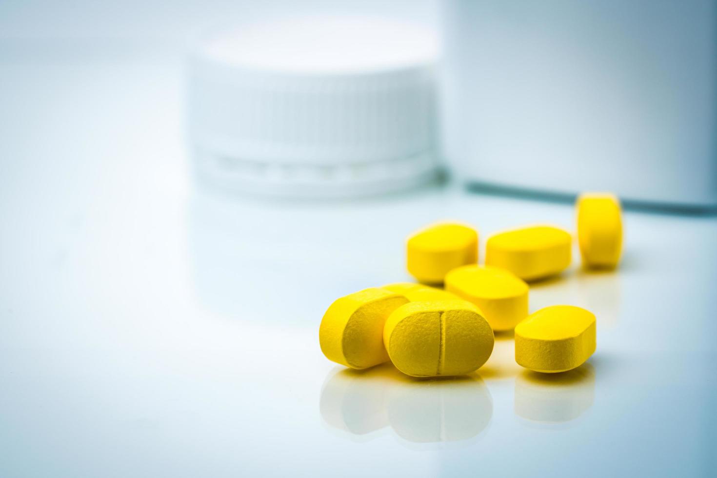 Pile of yellow tablets pills on blurred background of plastic pills bottle with copy space. Ibuprofen for relief pain, headache, high fever and anti-inflammatory. Closeup of painkiller caplets pills. photo