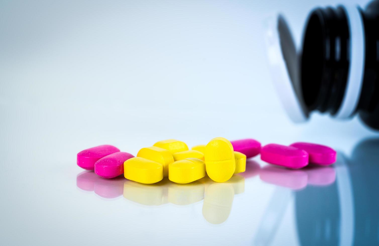 Yellow and pink oval tablet pills with shadows on white background with blurred pills bottle. Mild to moderate pain management. Pain killer medicine. Ibuprofen caplets pills. photo