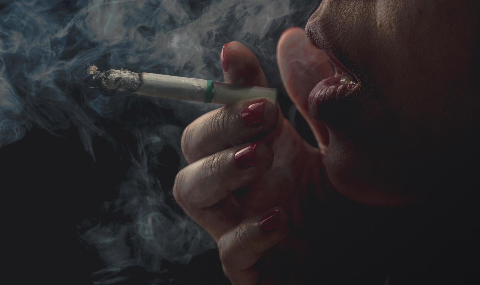 Woman with red nail is smoking cigarette on dark background. Quit smoking concept. Bad habit in woman can cause aging and lung cancer. Stressed woman. Nicotine addicted. 31 May World no tobacco day. photo