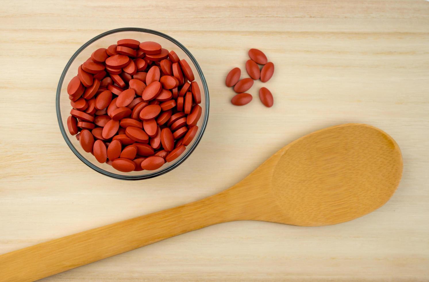 Top view of iron tablets in glass bowl and spatula on wood tray with copy space. Use for topics content about treatment anemia in adult, elderly people and children photo