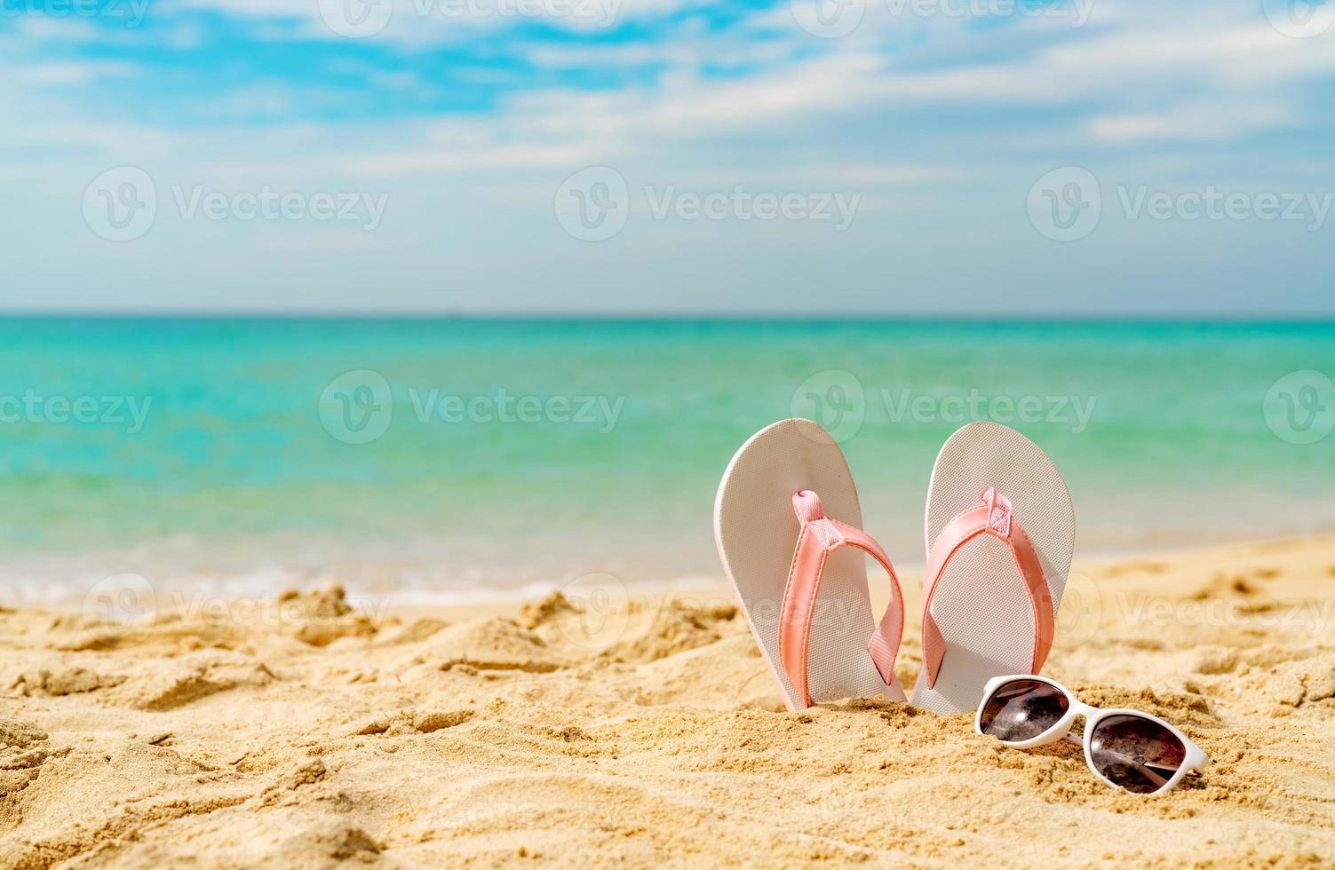 Pink and white sandals, sunglasses on sand beach at seaside. Casual fashion style flipflop and glasses. Summer vacation on tropical beach. Fun holiday travel on sandy beach. Summertime. Summer vibes. photo