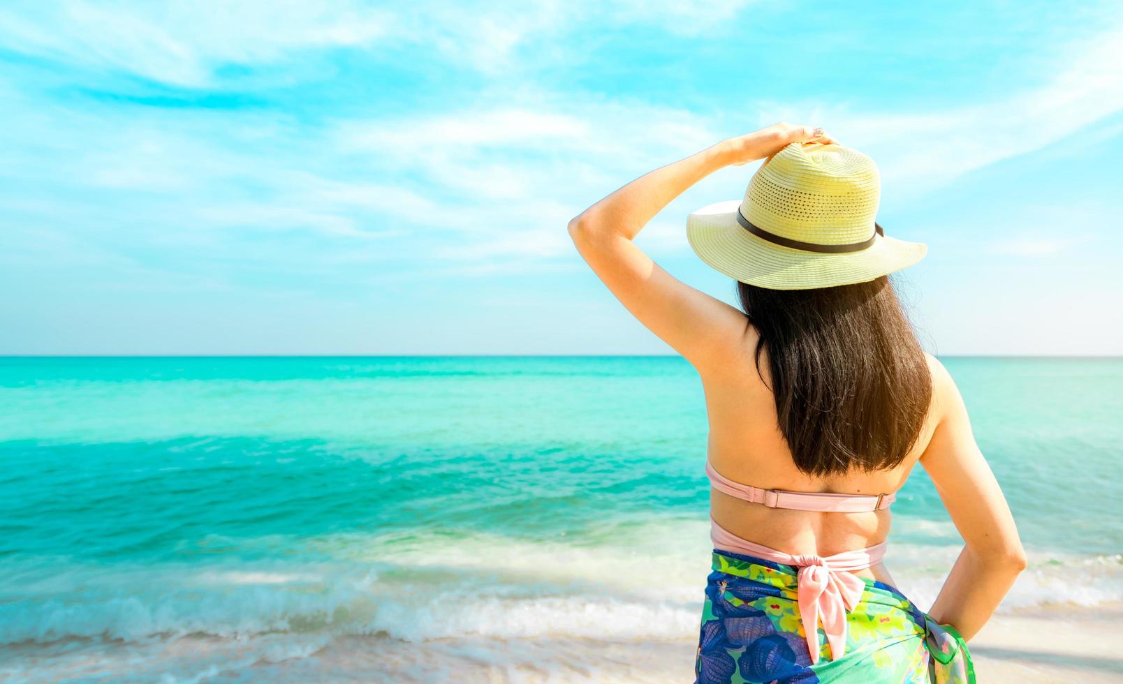 Back view of happy young Asian woman with straw hat relax and enjoy holiday at tropical paradise beach. Girl in summer vacation fashion. Beauty sexy model. Sand beach. Summer vibes. Summer travel. photo