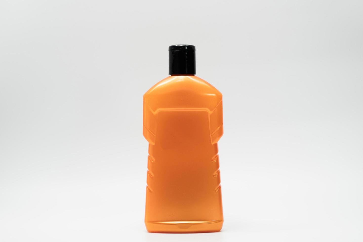 Orange color cosmetic bottle with black cap isolated on white background with copy space and blank label. Dandruff shampoo bottle with modern design. Personal hair and body care product in bathroom. photo