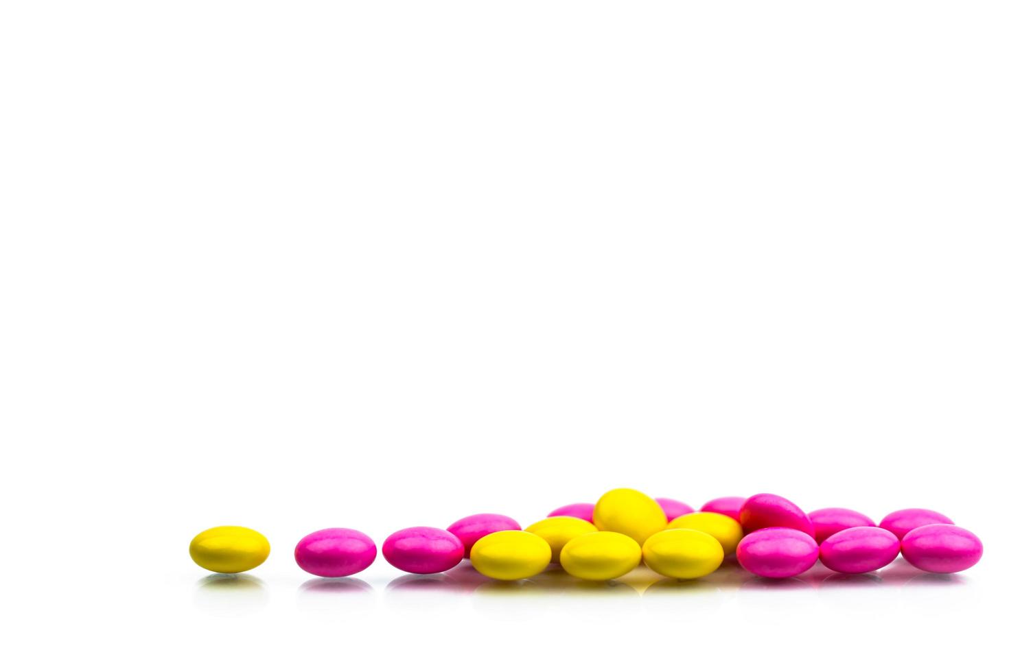 Pile of pink and yellow round sugar coated tablets pills isolated on white background with copy space. Colorful pills for treatment anti anxiety, antidepressant and migraine headache prophylaxis. photo