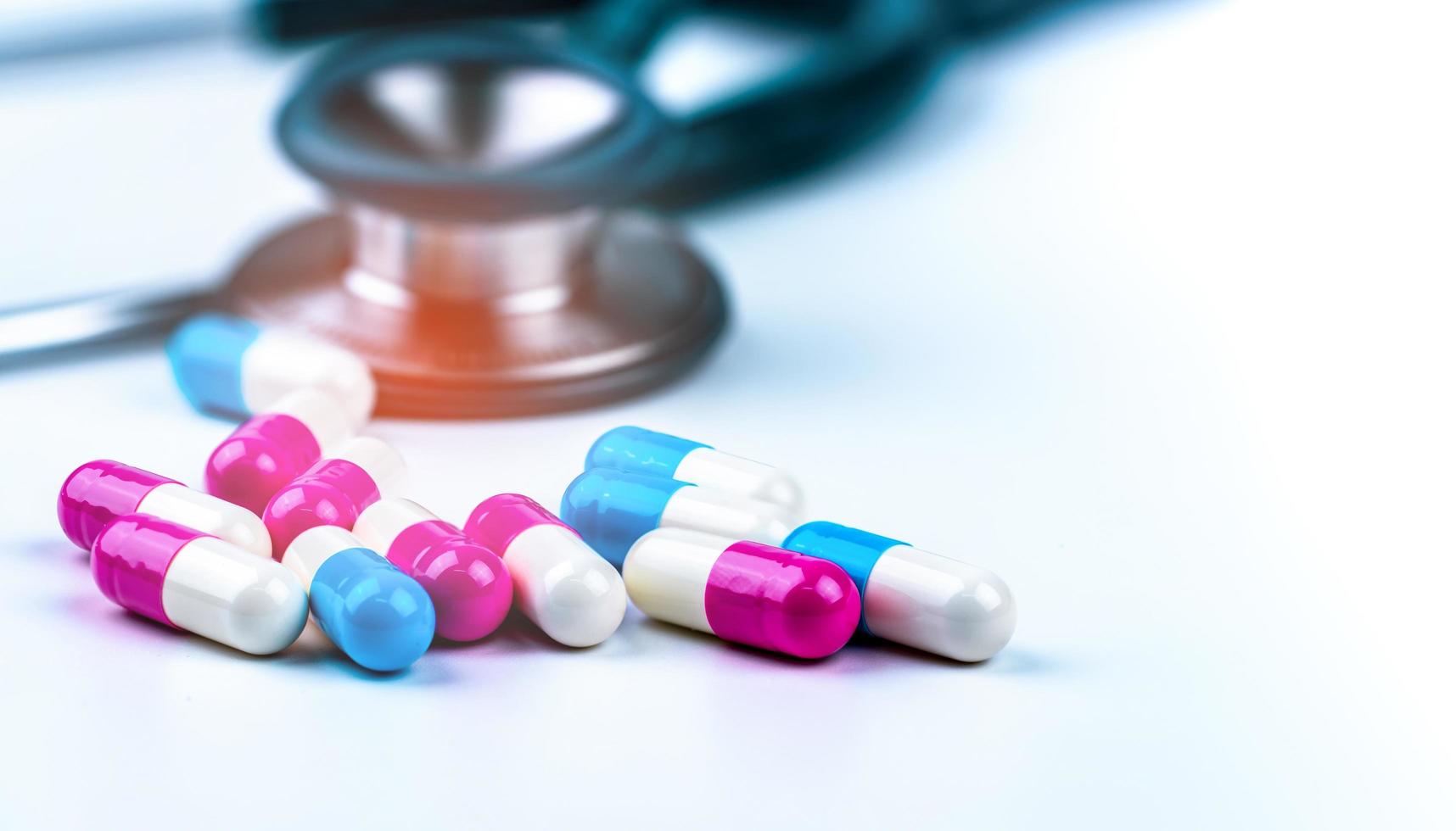 Green stethoscope with pile of antibiotic capsule pills on white table near drug tray. Antimicrobial drug resistance and overuse. Medical equipment for doctor. Clinical Cardiology concept. Health care photo