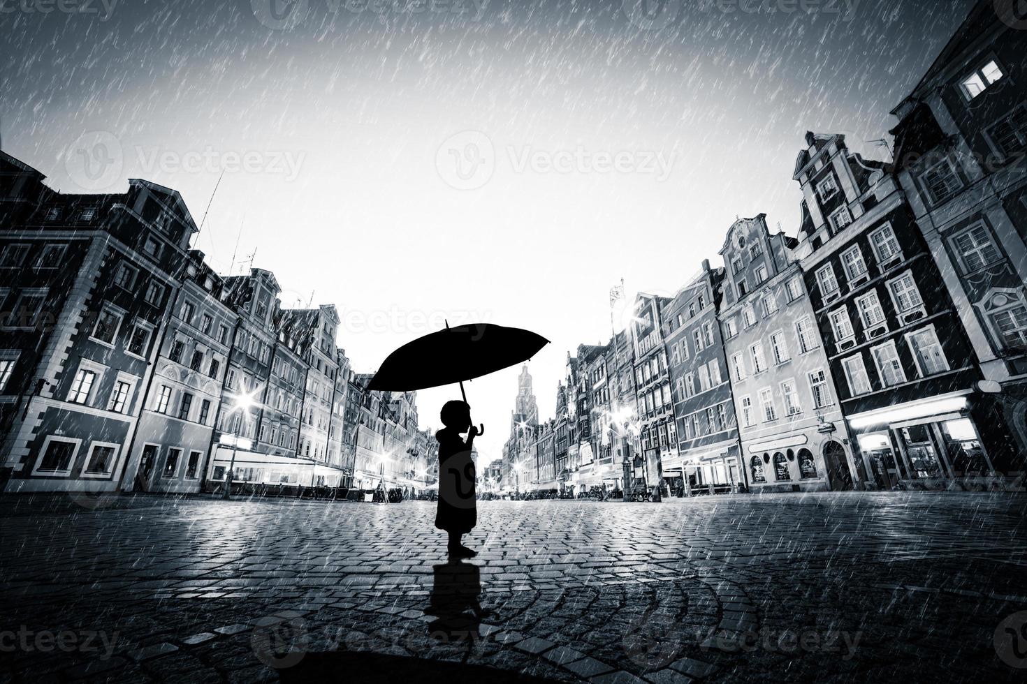 Child with umbrella standing alone on cobblestone old town in rain photo