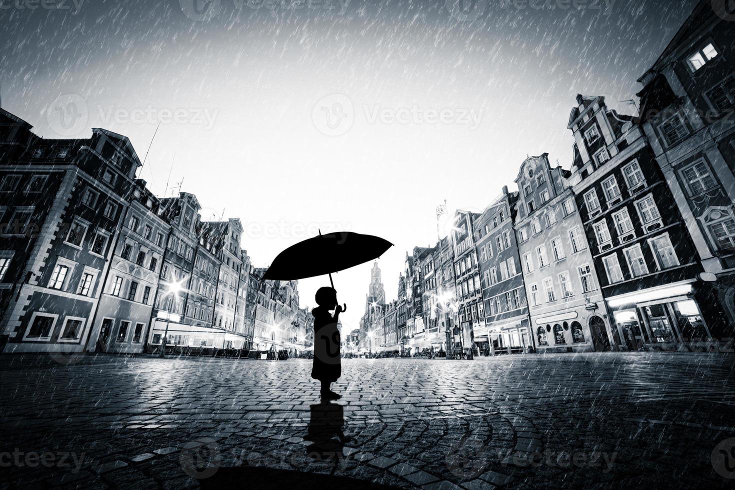 Child with umbrella standing alone on cobblestone old town in rain photo