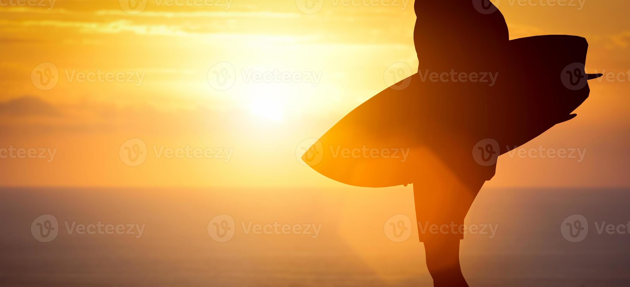 Surfer standing with his surfboard on the beach at sunset over the ocean photo