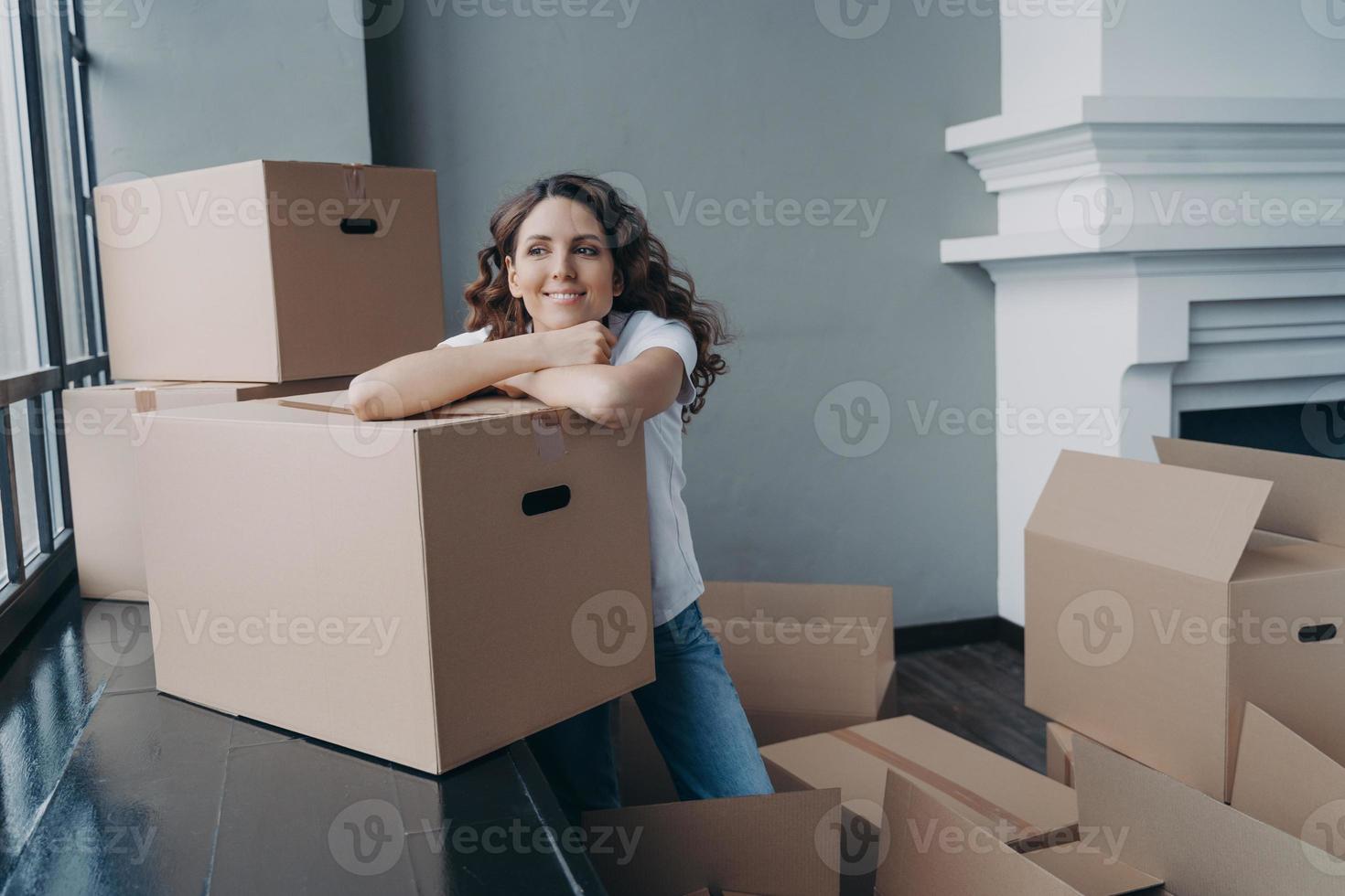 Young lady is dreaming while sitting on floor in new home. Large living room, window and fireplace. photo