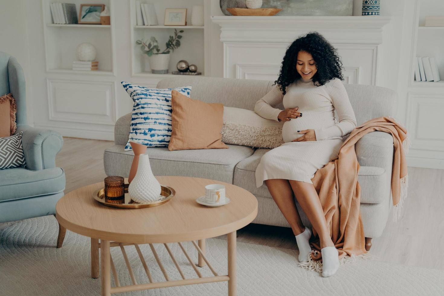 mujer afroamericana embarazada sentada en el sofá y pasando tiempo en casa foto
