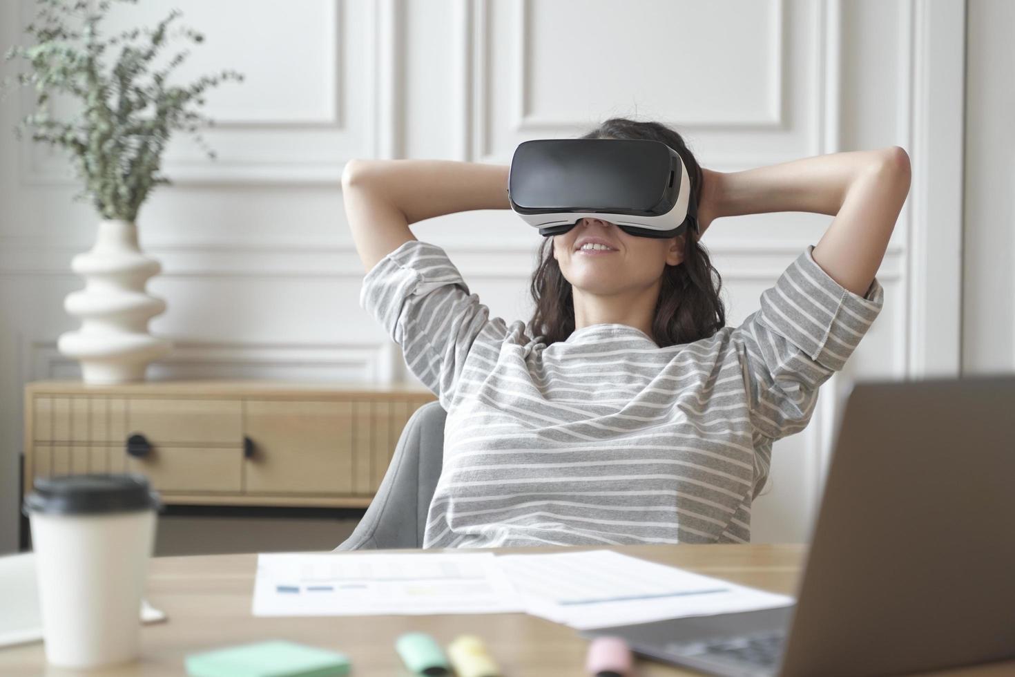 Relaxed young woman office worker in VR headset or helmet watching in 360 degrees video or movie photo
