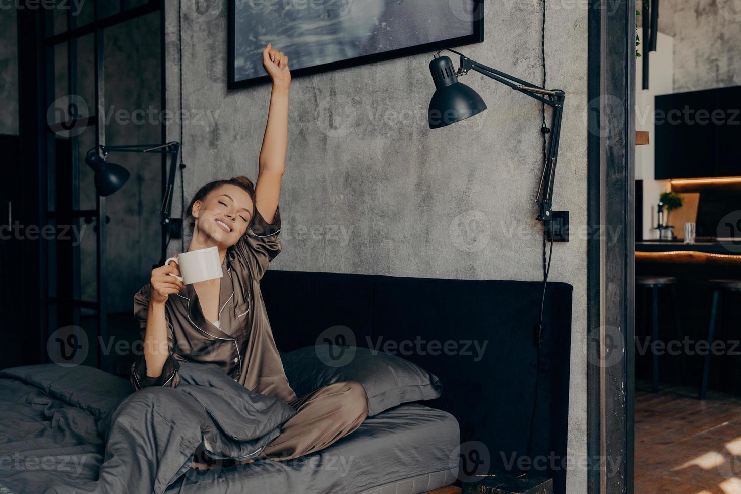 joven y hermosa mujer soñolienta con el pelo atado en un moño comenzando su mañana con una taza de café caliente foto