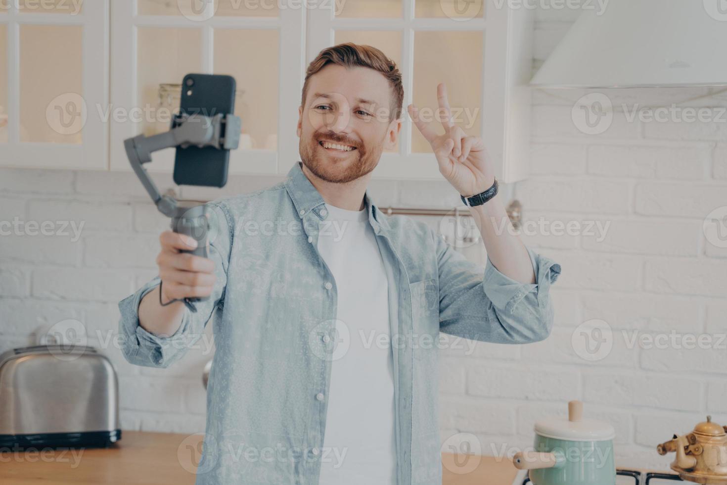 Handsome smiling young brunete man with stubble making selfie in kitchen photo
