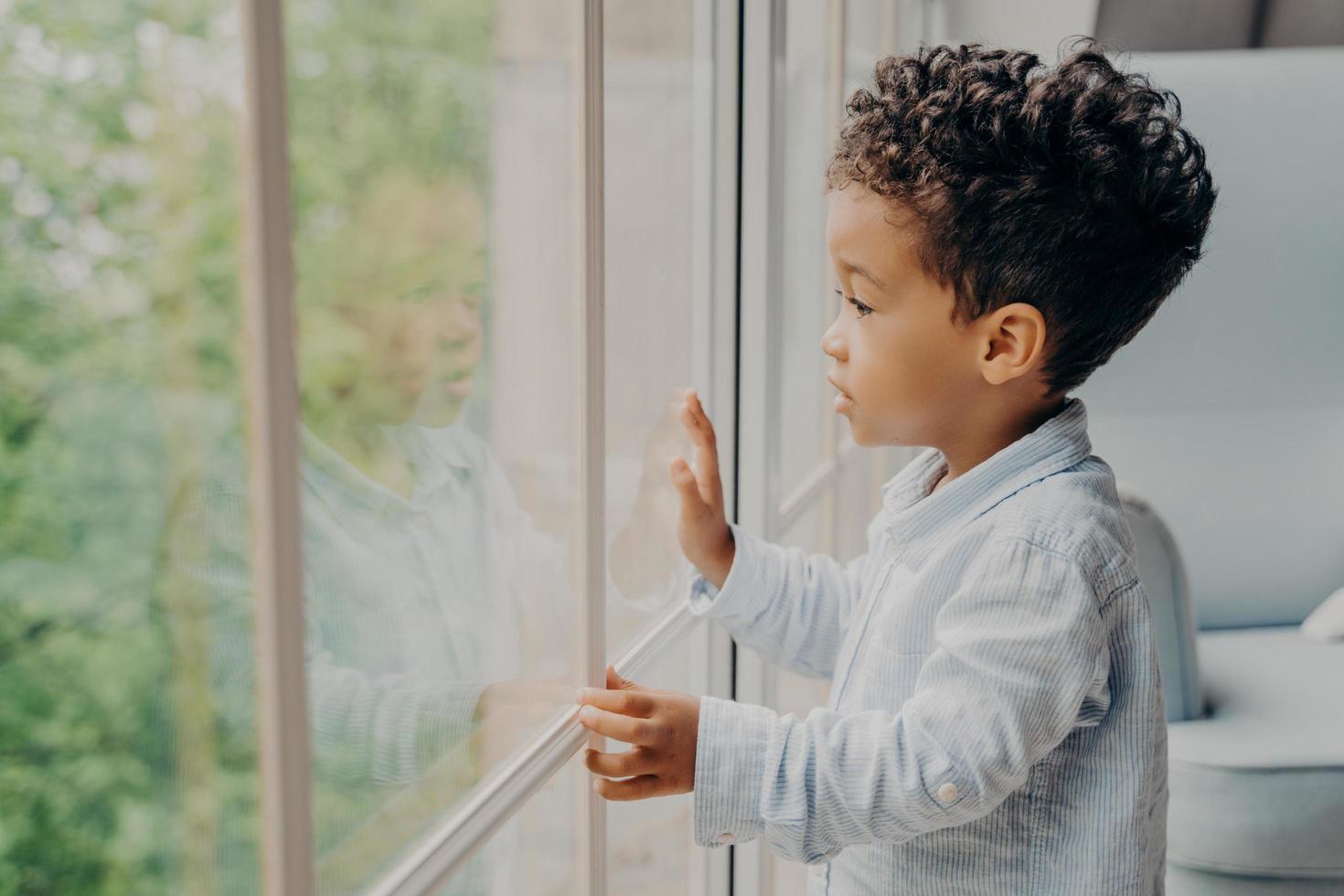 Sweet african american kid looking through window and waiting for parents photo