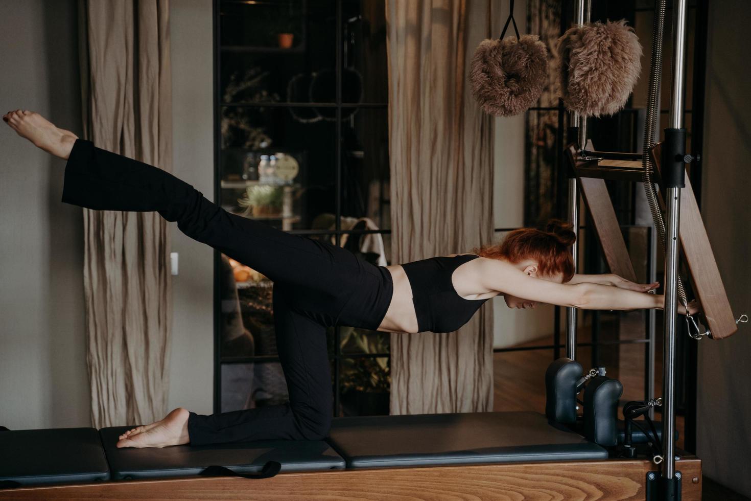 Young athletic woman exercising and stretching leg on pilates reformer photo