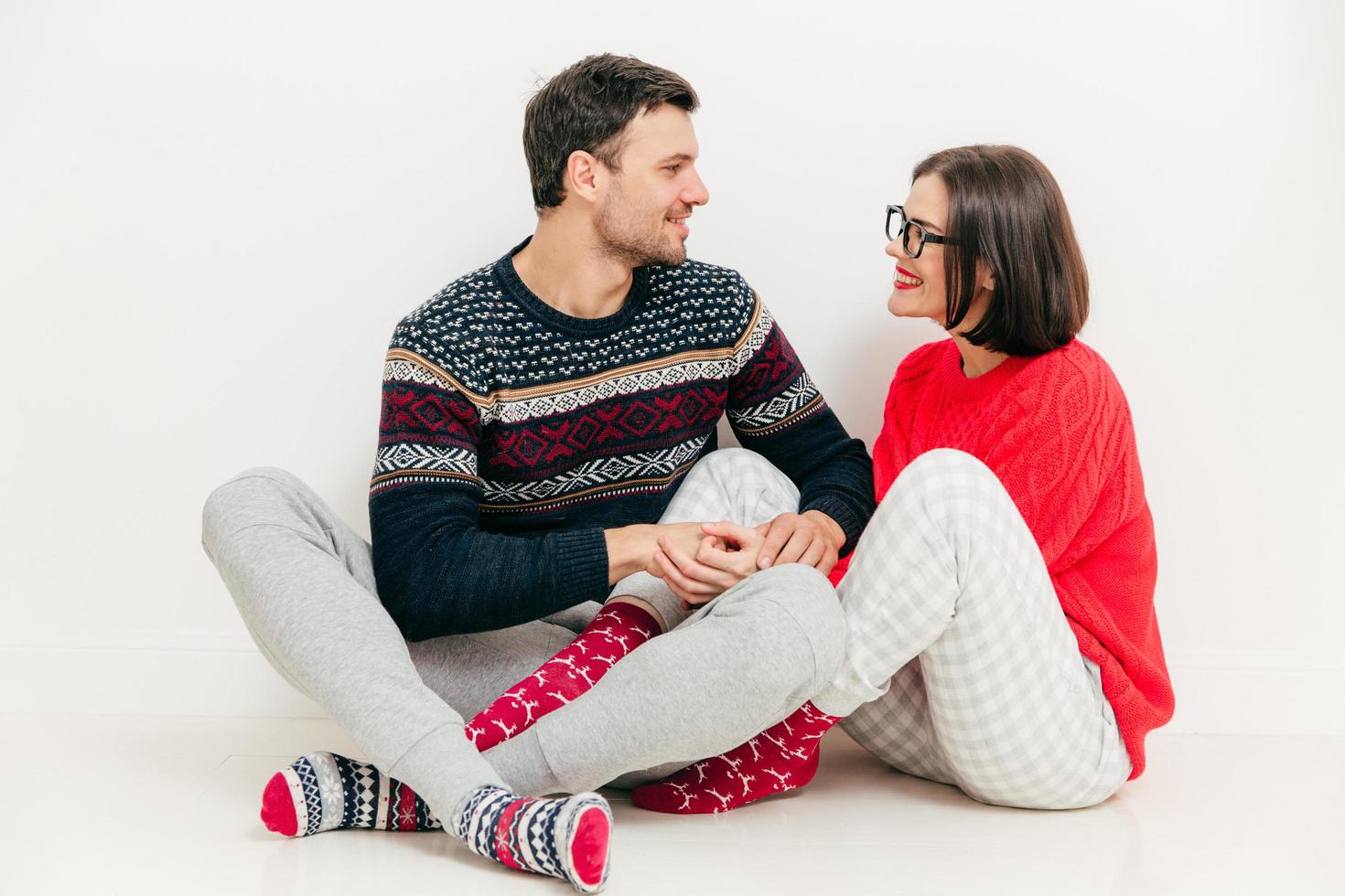 Romantic female and male hold hands together, look at each other with love, have good relationship, wears knitted sweaters, have positive expressions, isolated on white background. Relationship photo