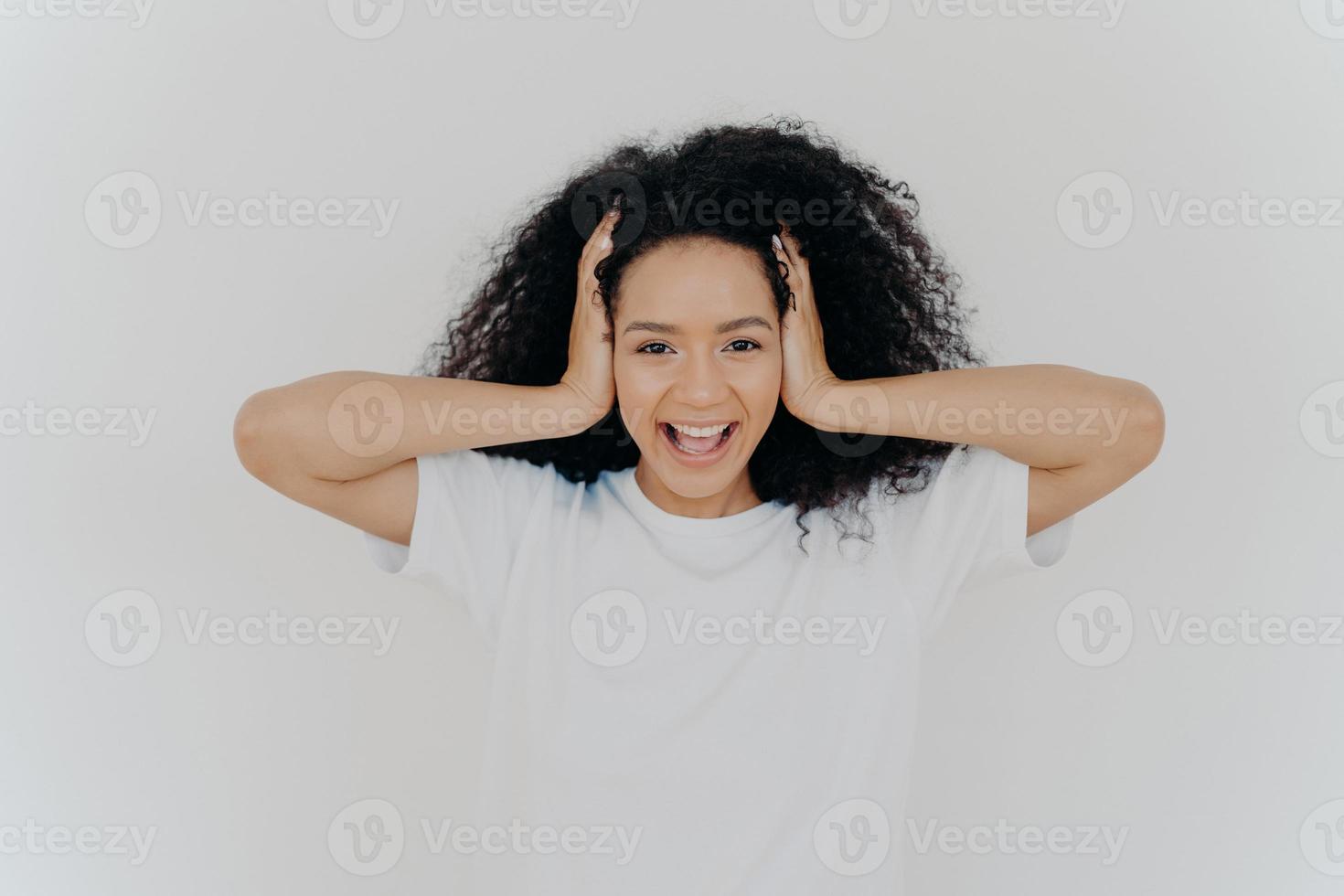 Photo of joyful dark skinned woman keeps hands on head, curly hair, laughs from joy, excited from positive emotions, dressed in white t shirt, hears funny joke, laughs sincerely. People, emotions 7799625 Photo of joyful dark skinned woman keeps hands on head, curly hair, laughs from joy, excited from positive emotions, dressed in white t shirt, hears funny joke, laughs sincerely. People, emotions 7799625