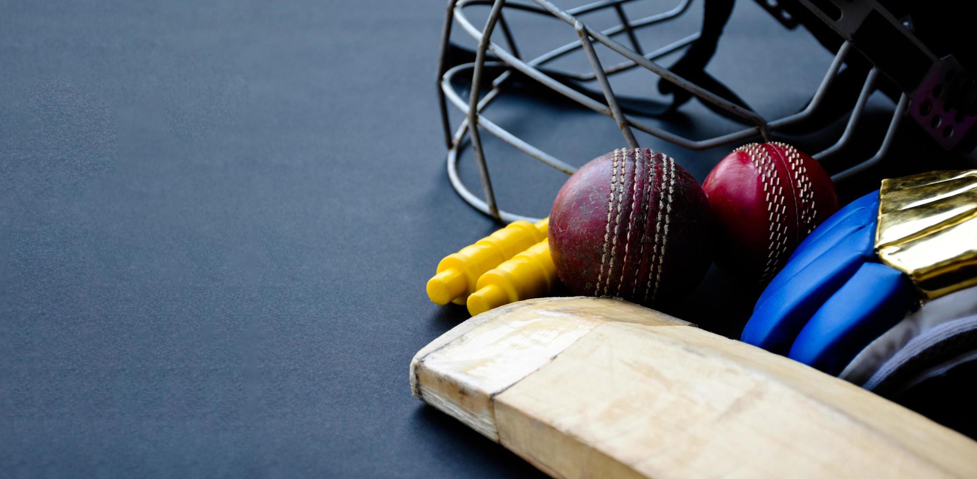 Old training cricket sport equipments on dark floor, leather ball, wickets, helmet and wooden bat, soft and selective focus, traditional cricket sport lovers around the world concept. photo