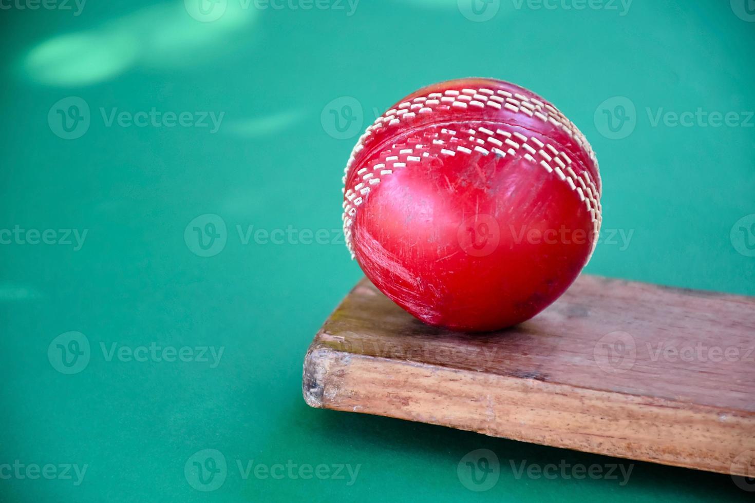 Closeup old cricket sport equipments on green floor, old leather ball, wooden bat, soft and selective focus, traditional cricket sport lovers around the world concept. photo