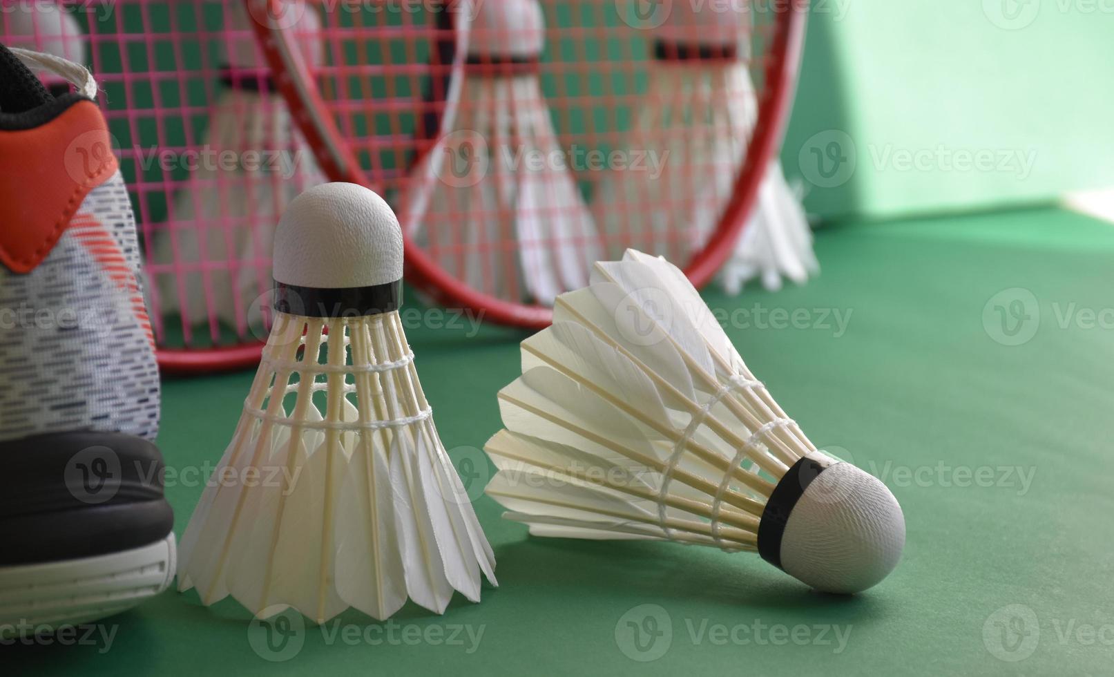 Badminton sport equipments on green floor of badminton court shuttlecocks, rackets, shoes, selective focus on shuttlecocks, badminton sport playing lover around the world concept. photo