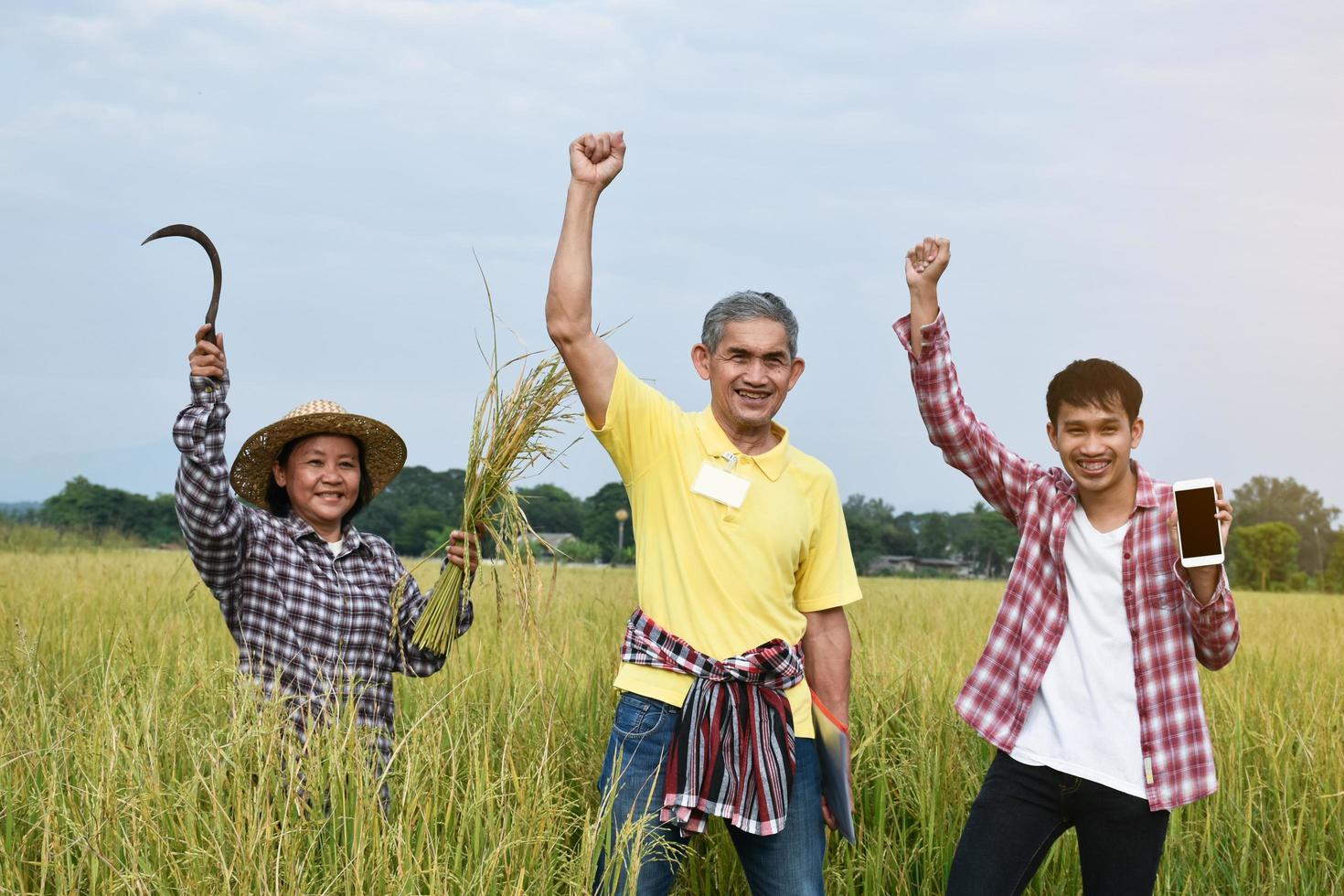 Three Asian farmers are standing in the rice paddy field and raising their hands to congratulate and rejoice at the successful completion of rice growing survey and data storing by using mobile phone. photo