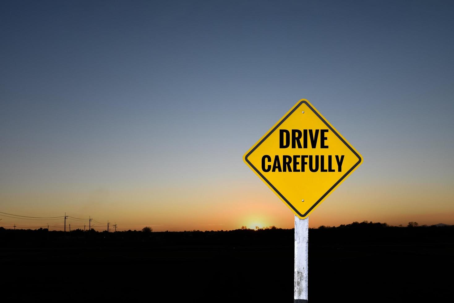 Yellow label traffic sign on white pole which has texts ' Drive carefully' with blurred sunset background, concept for informing drivers to drive vehicles at nighttime carefully around the world. photo