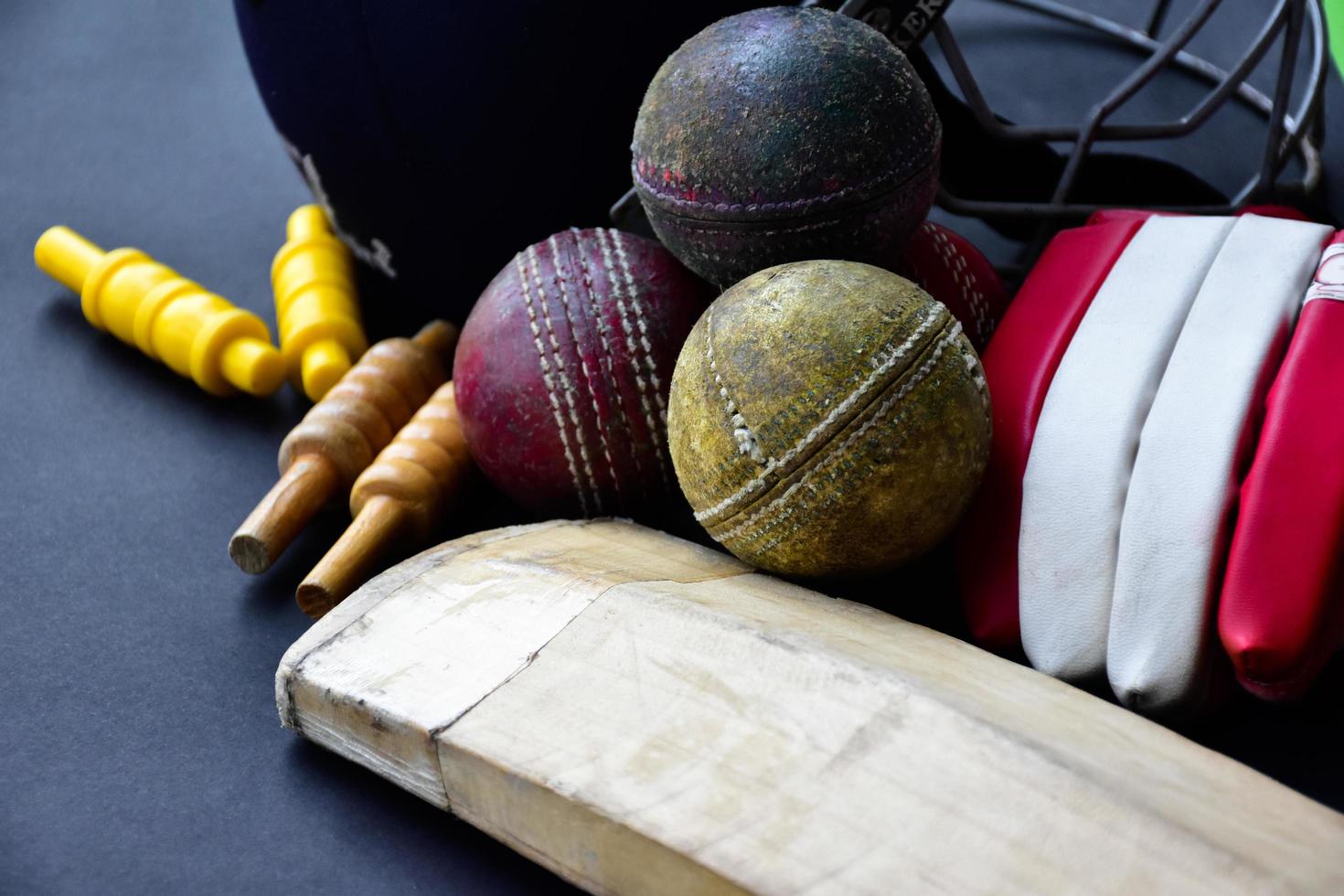 Old training cricket sport equipments on dark floor, leather ball, wickets, helmet and wooden bat, soft and selective focus, traditional cricket sport lovers around the world concept. photo