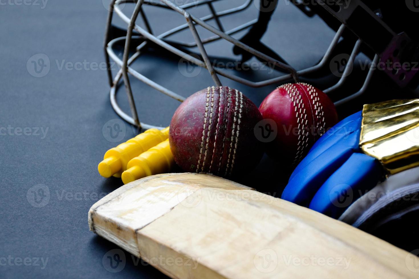 antiguos equipos deportivos de cricket de entrenamiento en suelo oscuro, pelota de cuero, wickets, casco y bate de madera, enfoque suave y selectivo, concepto tradicional de amantes del deporte de cricket en todo el mundo. foto