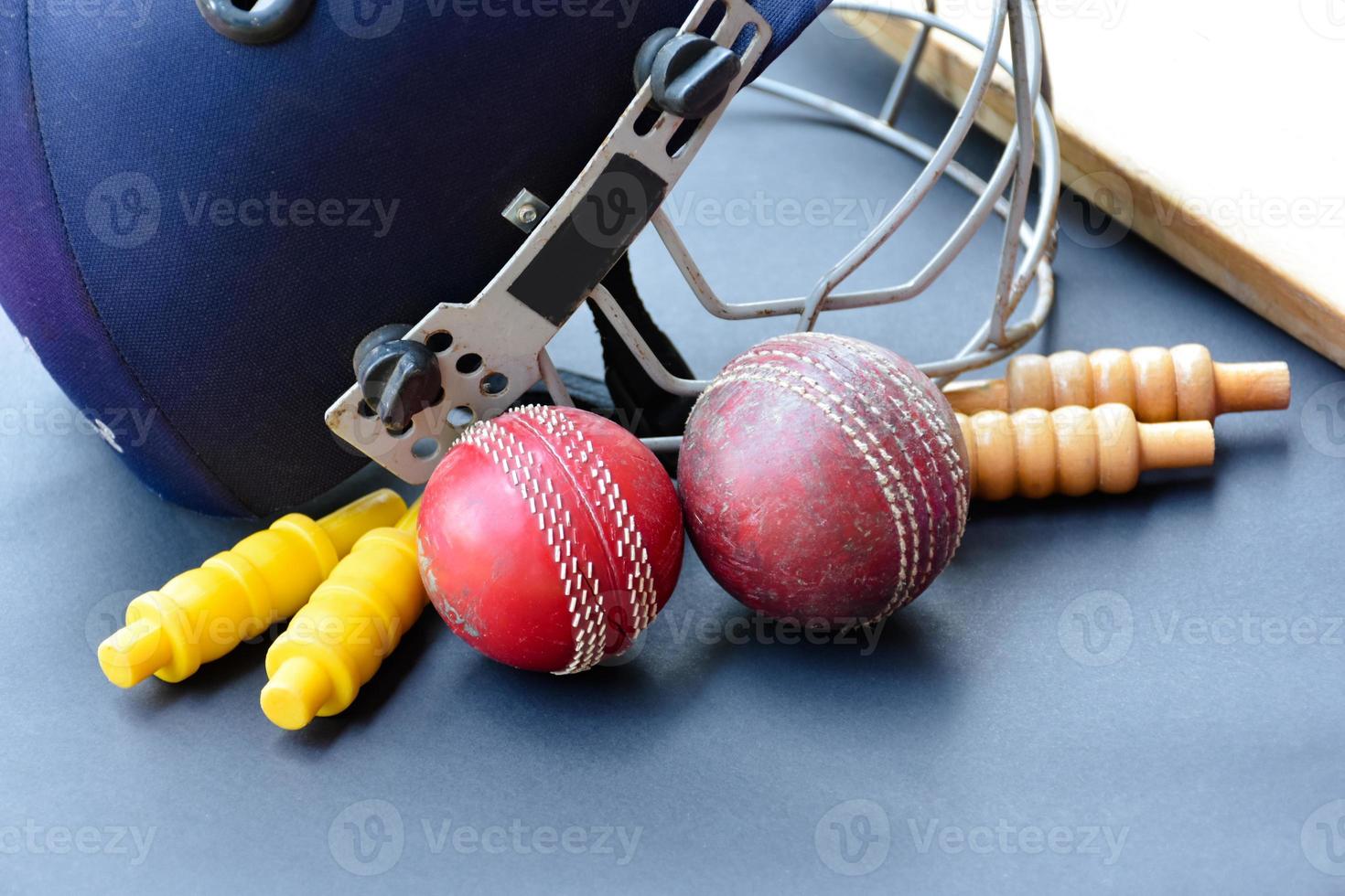 Old training cricket sport equipments on dark floor, leather ball, wickets, helmet and wooden bat, soft and selective focus, traditional cricket sport lovers around the world concept. photo