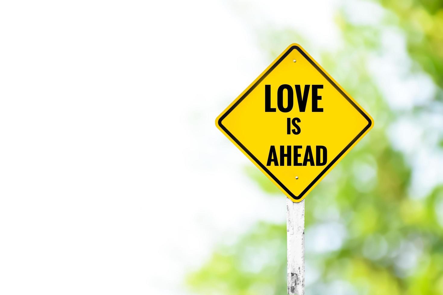 Yellow label traffic sign LOVE IS AHEAD on cement pole beside the rural road with blurred background, copy space, concept for informing  drivers drive carefully because there are lovers waiting. photo