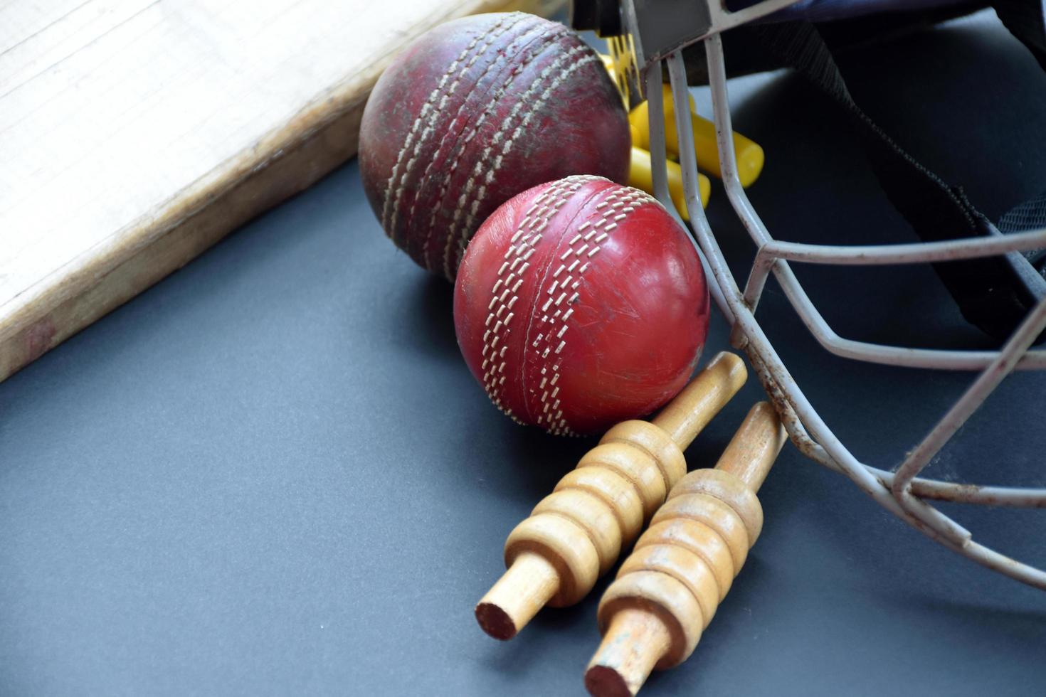 Old training cricket sport equipments on dark floor, leather ball, wickets, helmet and wooden bat, soft and selective focus, traditional cricket sport lovers around the world concept. photo